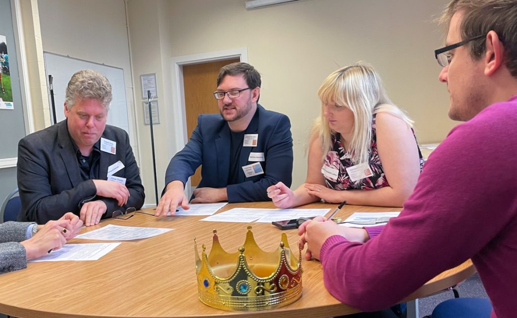 The Prince of Wales, James Hamilton, Becky as Henrietta Maria and the King, sat at a table in discussion