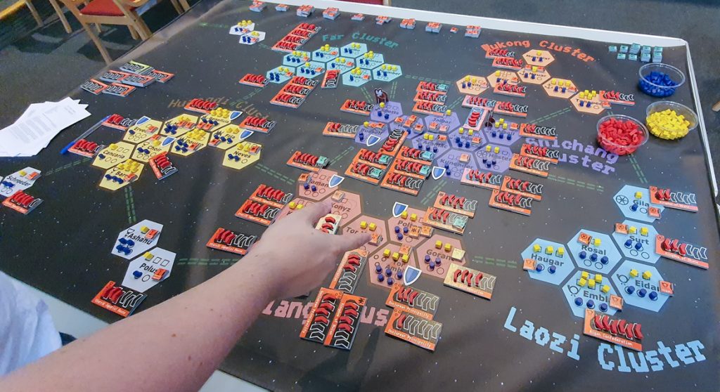 A colourful map covered in counters, with players standing around it