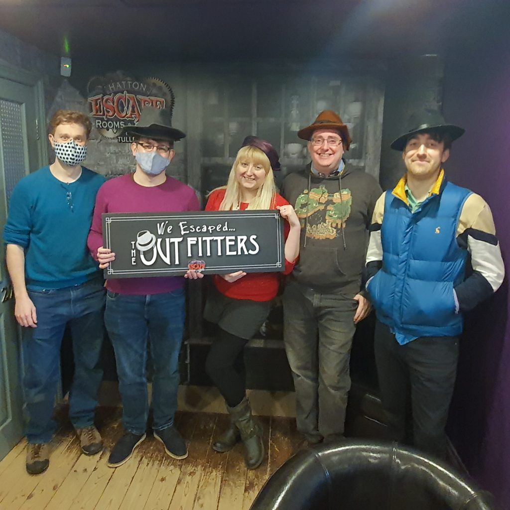Five people wearing hats, Becky in the centre, holding a sign: "We Escaped The Outfitters"
