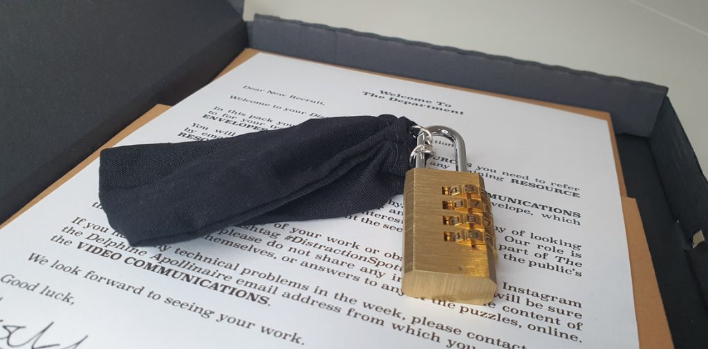 A black bag locked with a padlock, on top of a letter inside a box