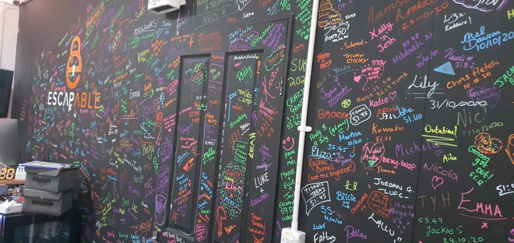 A black wall covered in neon writing: names of previous players