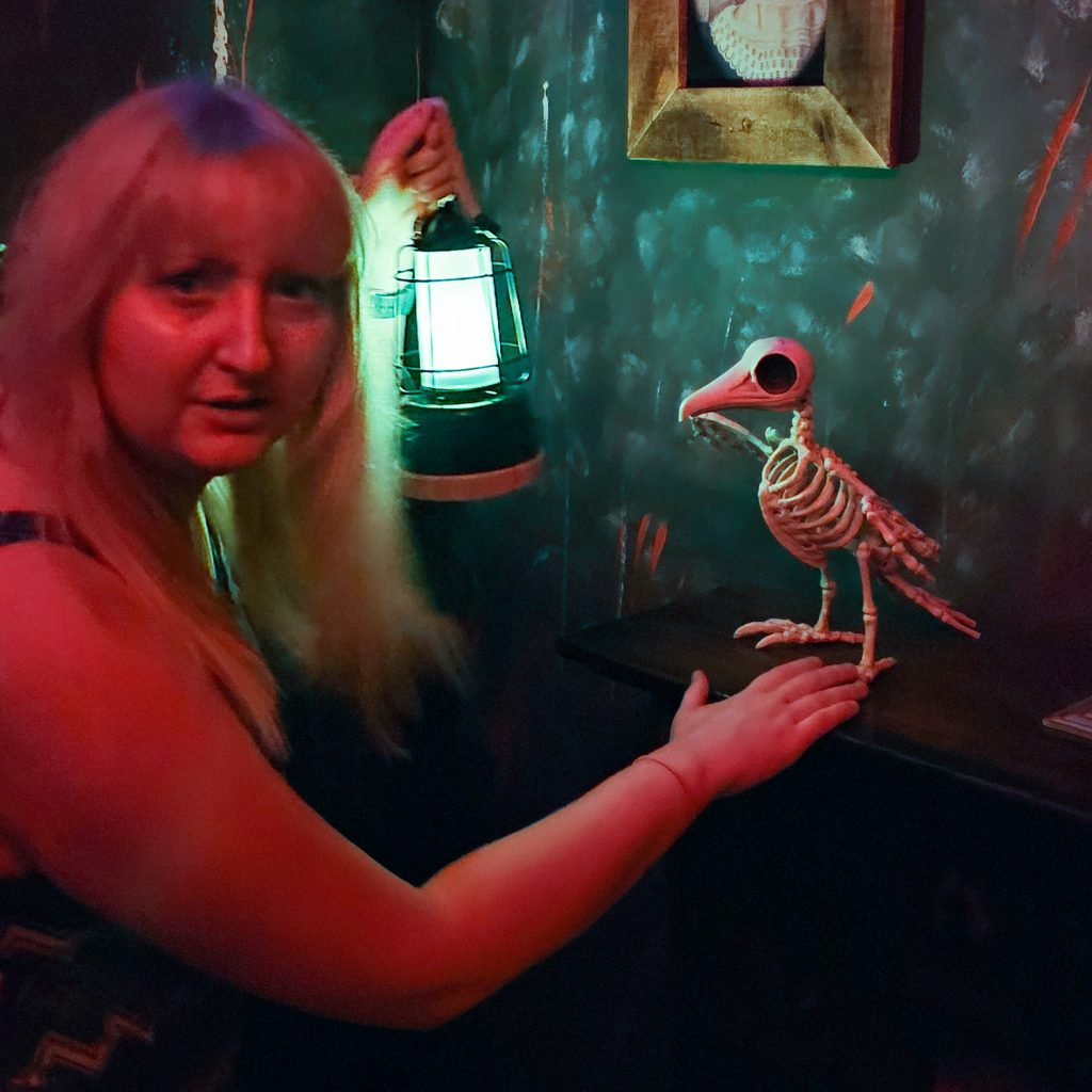 Becky looking concerned and holding up a lantern next to a fake bird skeleton