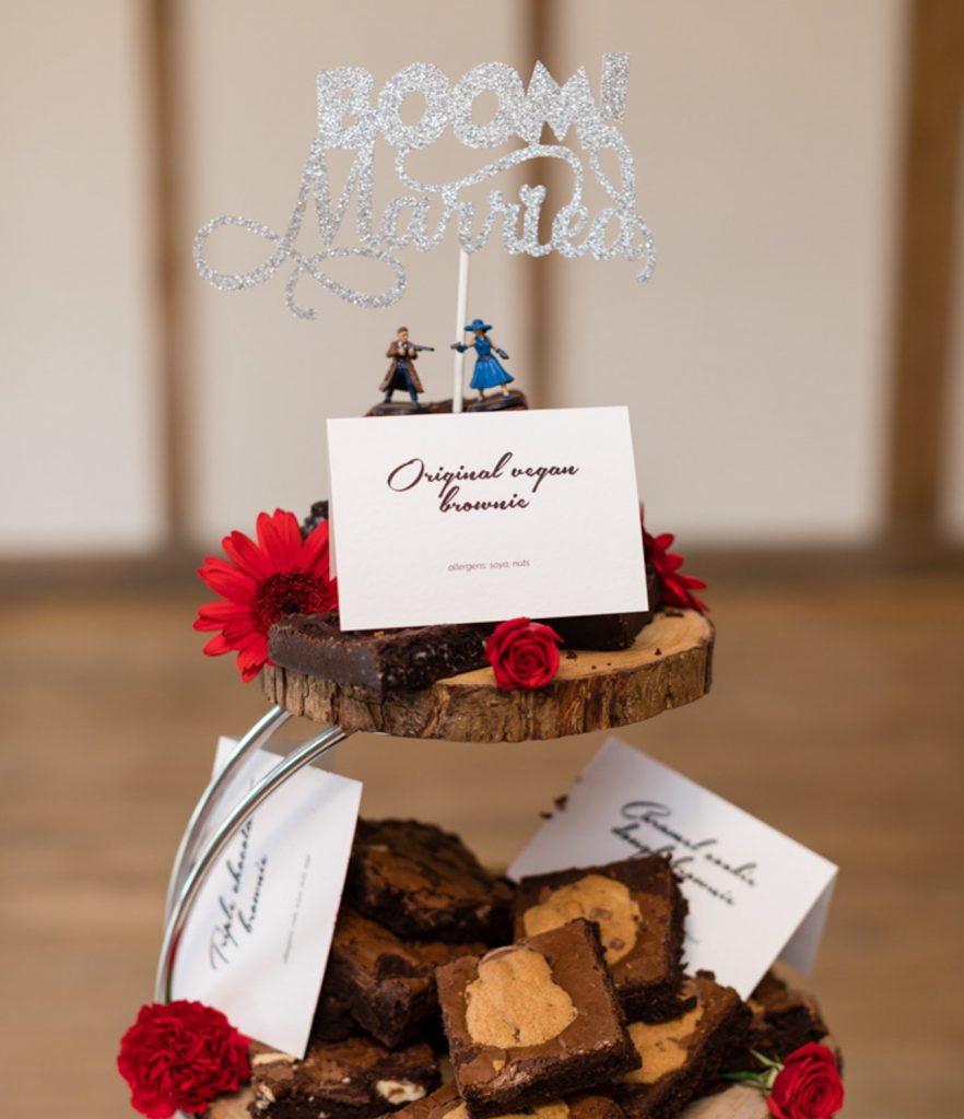 Two small figurines on top of brownies on a cake tower, with a sign reading "Boom Married" above them