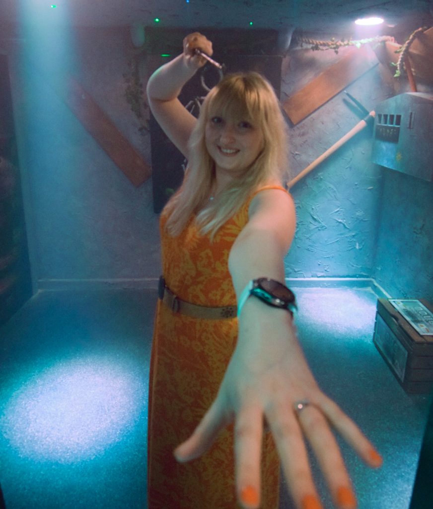 Becky reaching towards the camera with one hand, brandishing a magic wand above her head with the other