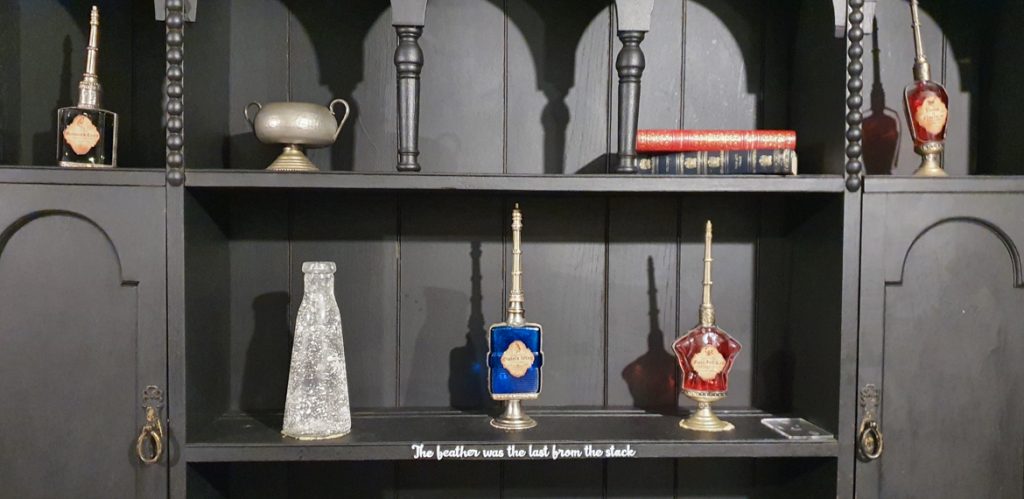 Shelves full of strange objects, including flasks, books and a strange encscription