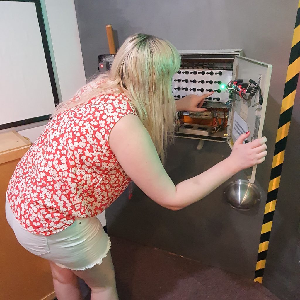 Becky bent down and fiddling with switches inside a wiring box